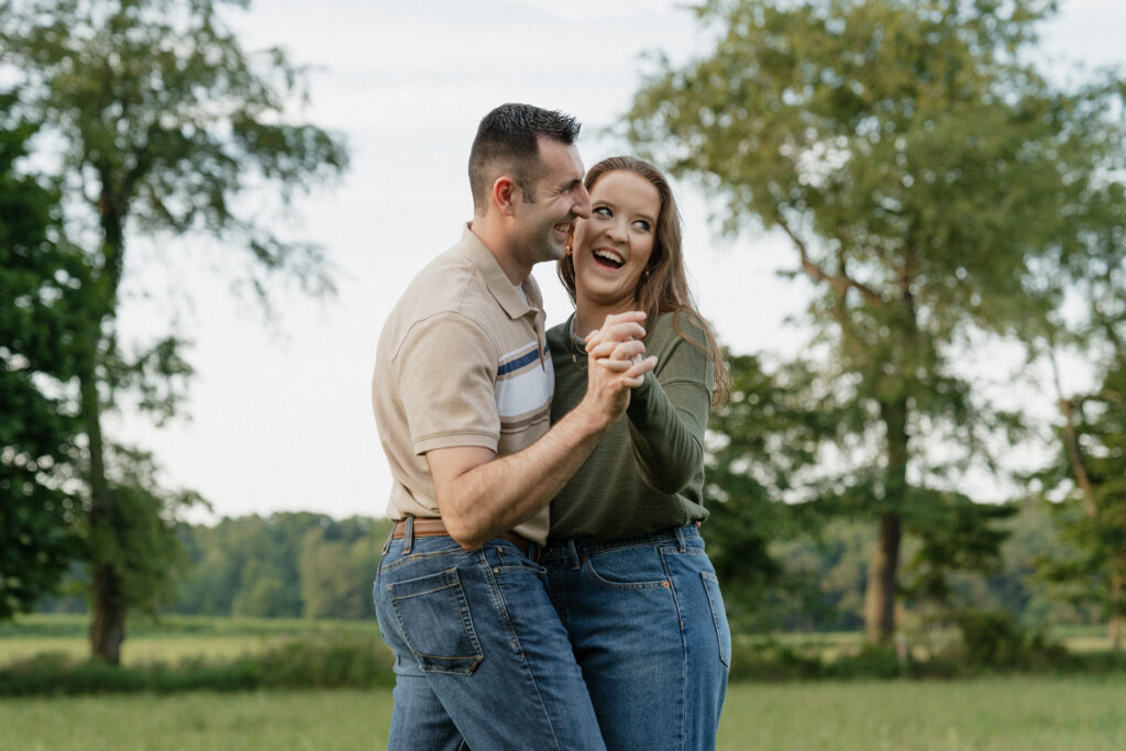 Couple laughs together while dancing in a field at golden hour