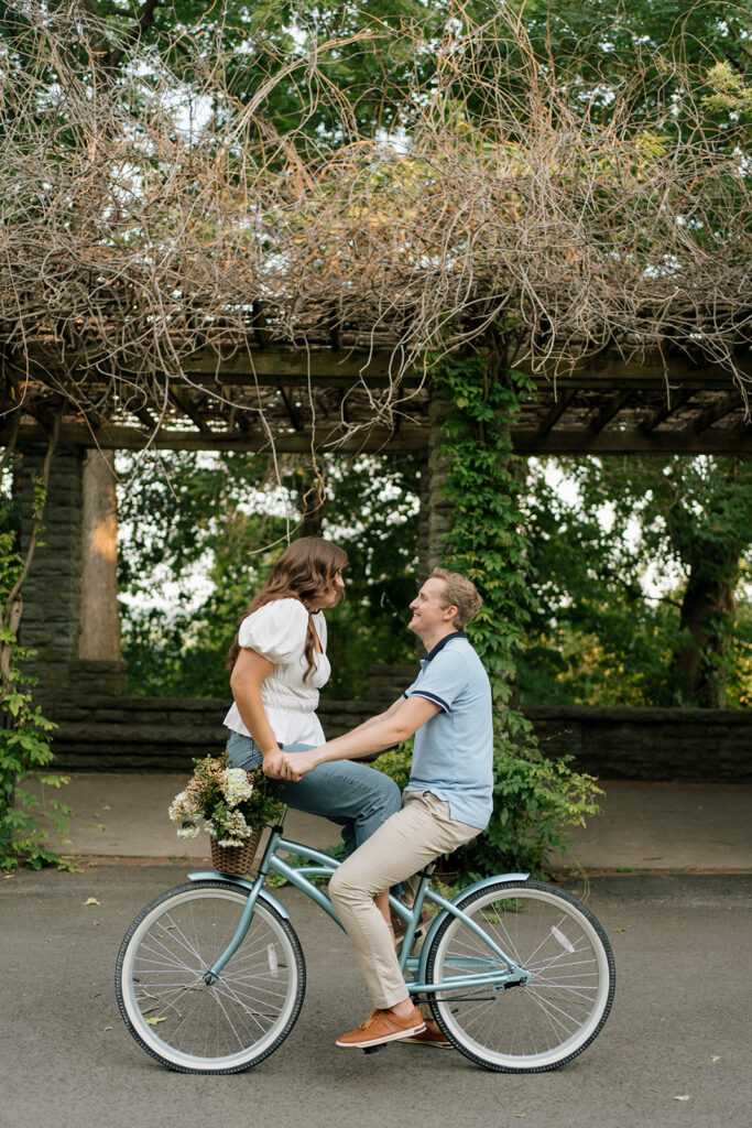 Couple looks at each other while riding a bike through a beautiful garden