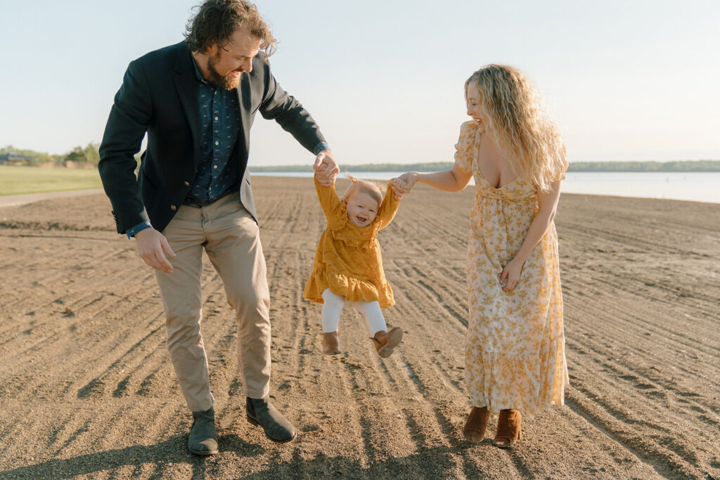 Mom and dad swing little daughter in between them as they walk along the beach