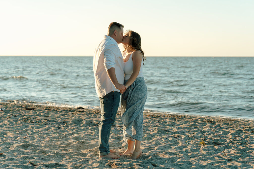 Couple kisses while wind blows on beach at sunset