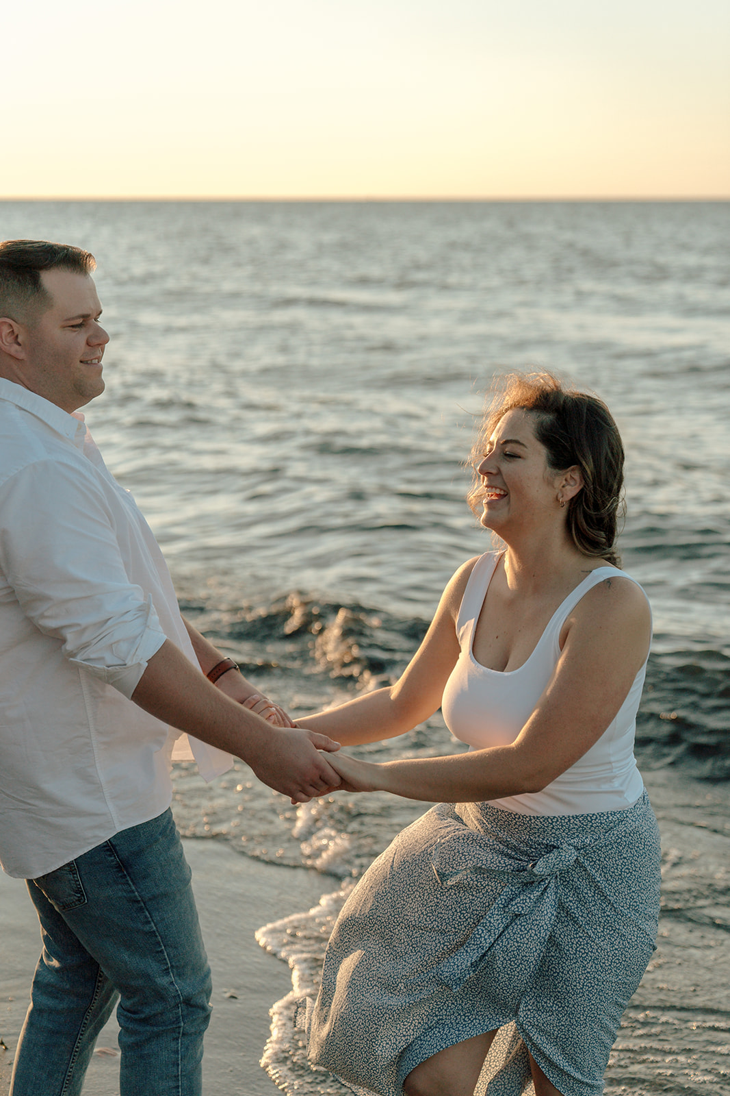 Engaged couple dance around the beach together at sunset during engagement photo shoot