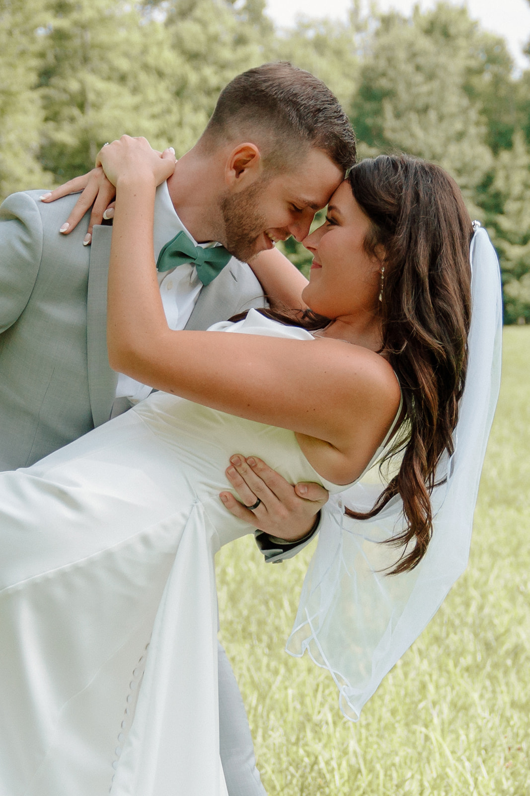 Groom and bride smile at each other nose-to-nose as they dip during wedding portraits