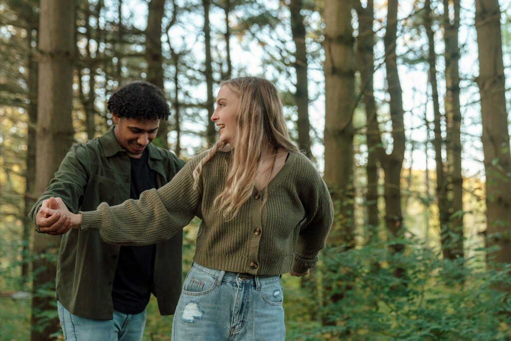 Couple laughs together while balancing on a log in the woods during couple photoshoot