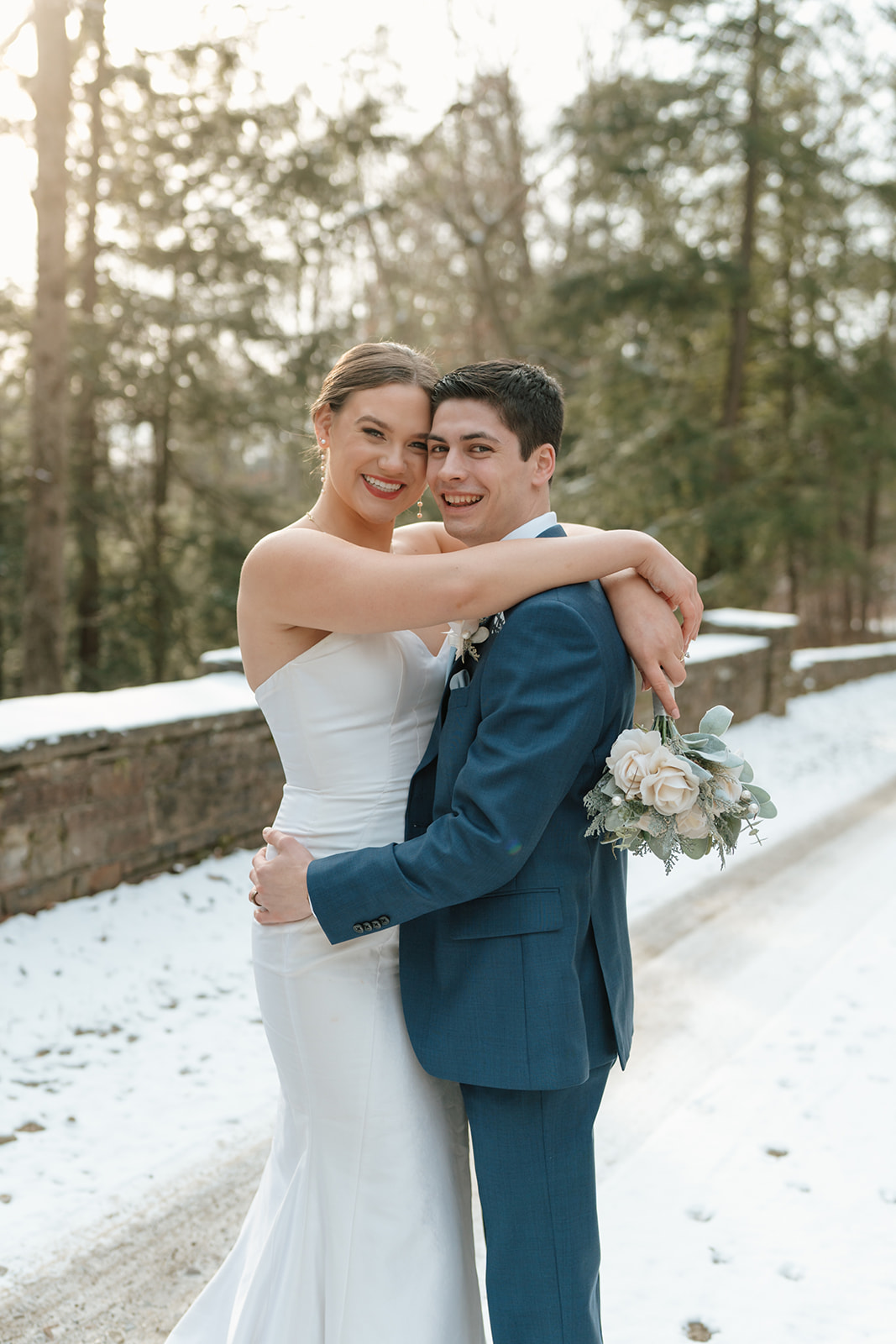 Bride and groom smile at the camera on their winter wedding day in the snow in Chagrin Falls, Ohio