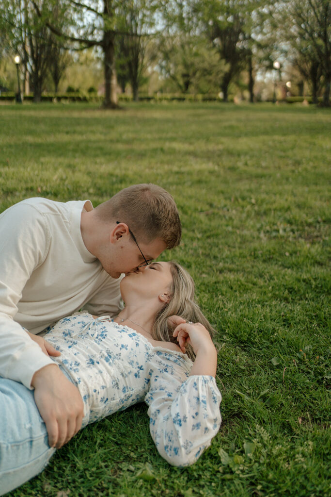 Engaged couple kisses while laying together in a grassy park