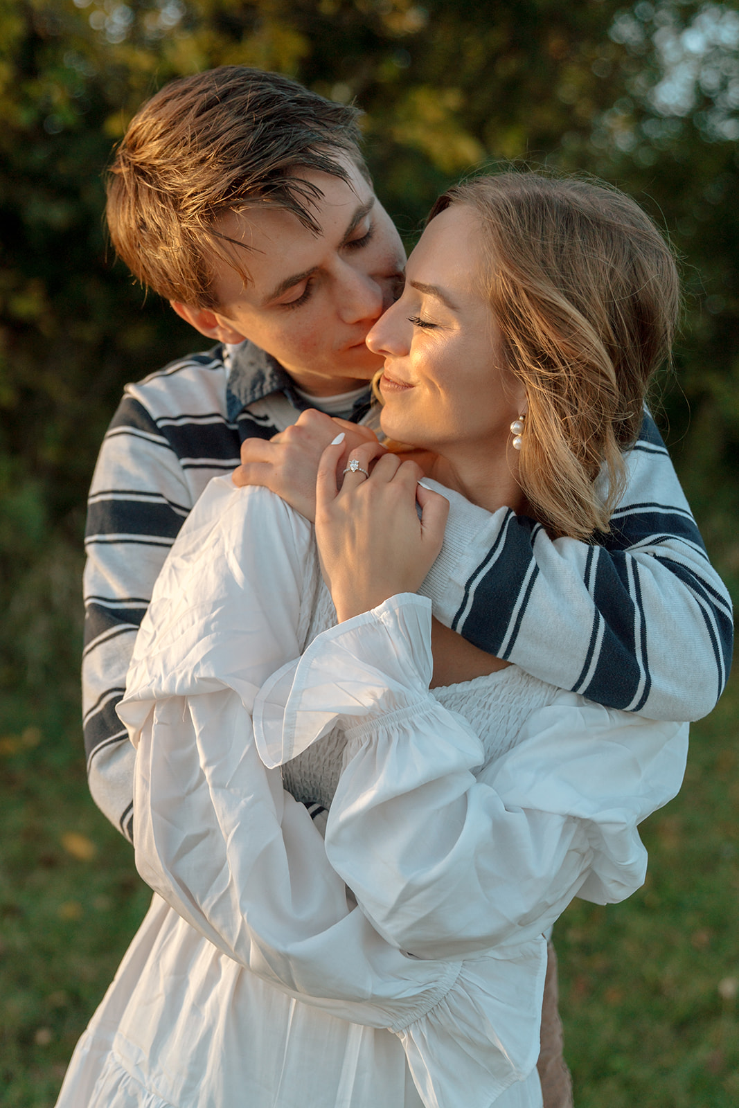 Man kisses bride-to-be on the cheek during engagement session at sunset