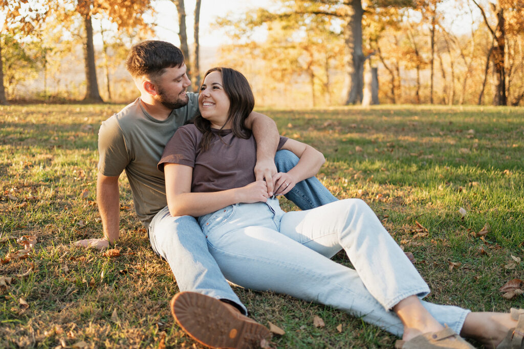 Engaged couple sits cuddling together in the grass in the fall