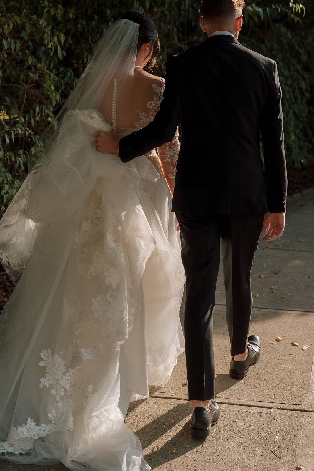 Bride and groom walk together at sunset while sun illuminates bride's veil and train