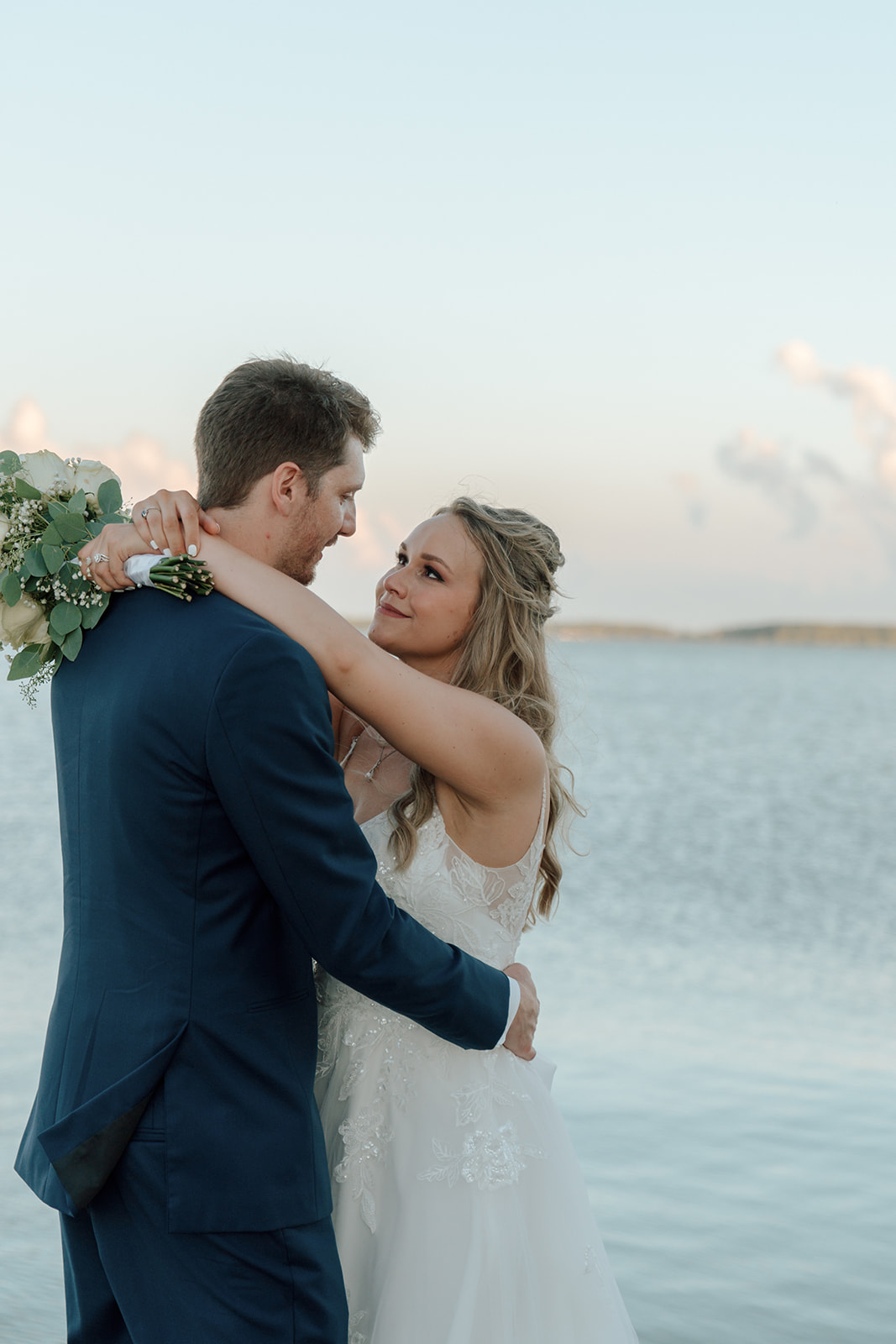 Bride and groom hold each other close with water and sunset in the background in Celina Ohio