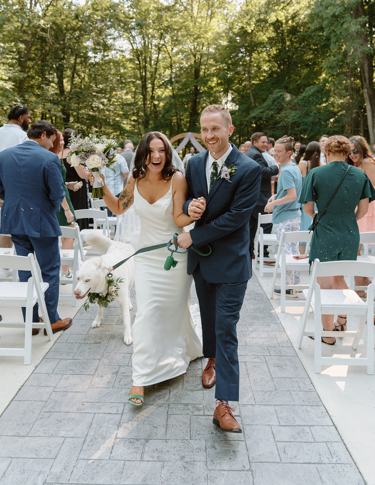 Bride and groom and their dog celebrate as they walk down the aisle while guests throw flower petals