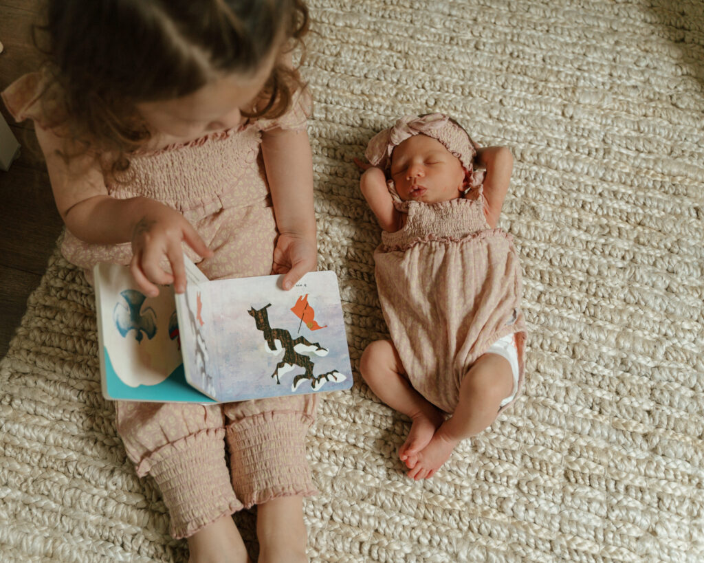 Toddler reads baby book to newborn sister during in home newborn photoshoot