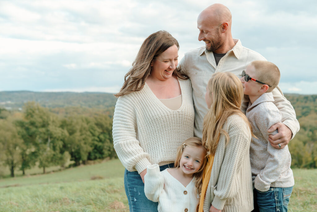 Family of five laugh together while standing on a hillside during family photo session